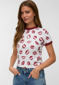 Hvid kortærmet t-shirt med en rund maroon halsudskæring, prydet med et gentaget design af røde læber. Båret med høj sombrero denim jeans.