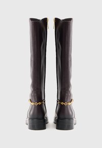 Bottes en cuir jusqu'aux genoux de couleur violet foncé avec un accent en chaîne dorée et un talon carré. Fermeture éclair à l'arrière, texture lisse.