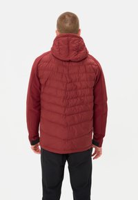 Giacca isolante rossa con cappuccio, caratterizzata da un design trapuntato e polsini elasticizzati. Indossata sopra pantaloni scuri, vista da dietro.