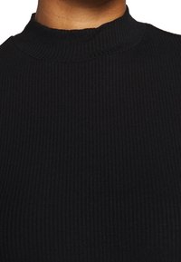 Czarny sweter z prążkowanym golfem, z wysokim, okrągłym kołnierzem i strukturalnym materiałem, zbliżenie uwydatniające jego wzór i miękkość.