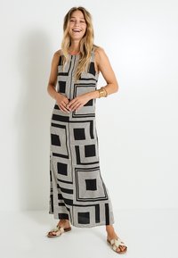 Robe maxi sans manches en noir et crème avec des motifs géométriques carrés. Tissu doux, coupe décontractée, fentes latérales et encolure arrondie.