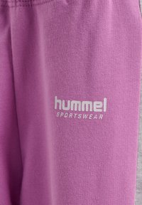 Lila sportbyxor i mjukt tyg, med "hummel"-logotyp i vitt. Har en texturerad yta och elastisk midja för komfort.