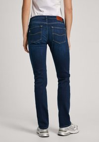 Mörkblå denimjeans med slim fit, med två bakfickor, diskret sömnad och en brun läderlapp i midjan.