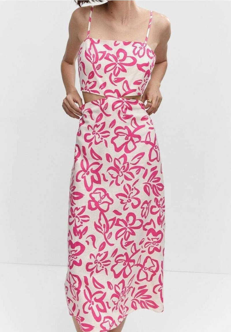 Femme portant une robe deux pièces blanche sans manches avec un motif floral rose, debout devant un fond clair uni.