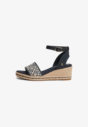 Sandale compensée avec semelle en jute tissée, bride avant à motif, bride de cheville noire avec boucle dorée et support de talon bleu marine.