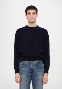 Pull en maille bleu marine avec un col rond côtelé, des manches longues et une coupe décontractée, associé à un jean bleu dans un délavage clair.