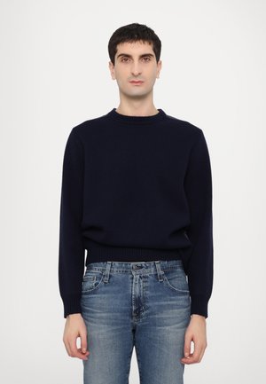 Pull en maille bleu marine avec un col rond côtelé, des manches longues et une coupe décontractée, associé à un jean bleu dans un délavage clair.