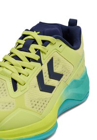 Jaskrawozielony but sportowy z granatowymi akcentami, cholewką z siateczki, sześciokątnym wzorem, teksturowaną gumową podeszwą i kontrastującą aqua podeszwą zewnętrzną.