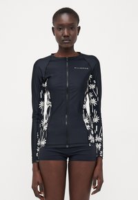 Langermet navy rash guard med glidelås foran, prydet med hvite palmetre-grafikker på ermene, laget av elastisk, hurtigtørkende stoff.