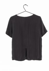 Blusa nera a maniche corte in tessuto liscio, con uno spacco laterale sul retro e un collo rotondo, appesa a un appendiabiti nero su sfondo bianco.