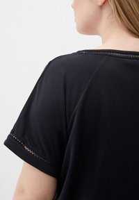 Černý top s krátkým rukávem a jemnou texturou, s výstřihem do U a dekorativní síťovinou na rukávech. Jednoduchý a univerzální design.