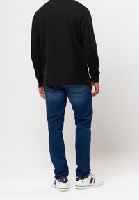 Maglietta nera a maniche lunghe abbinata a jeans blu, con taglio dritto. Sneakers bianche completano l'outfit, mostrando accenti di colore sulle scarpe.