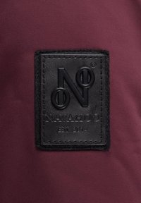 Patch en cuir noir avec le texte embossé "N" et "NAVAHOO EST 2014" sur un fond en tissu bordeaux.