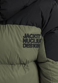 Doudoune noire et olive avec logo brodé "JACKIT NUCL1US DESIGN" en noir sur la section olive. Texture douce et matelassée.