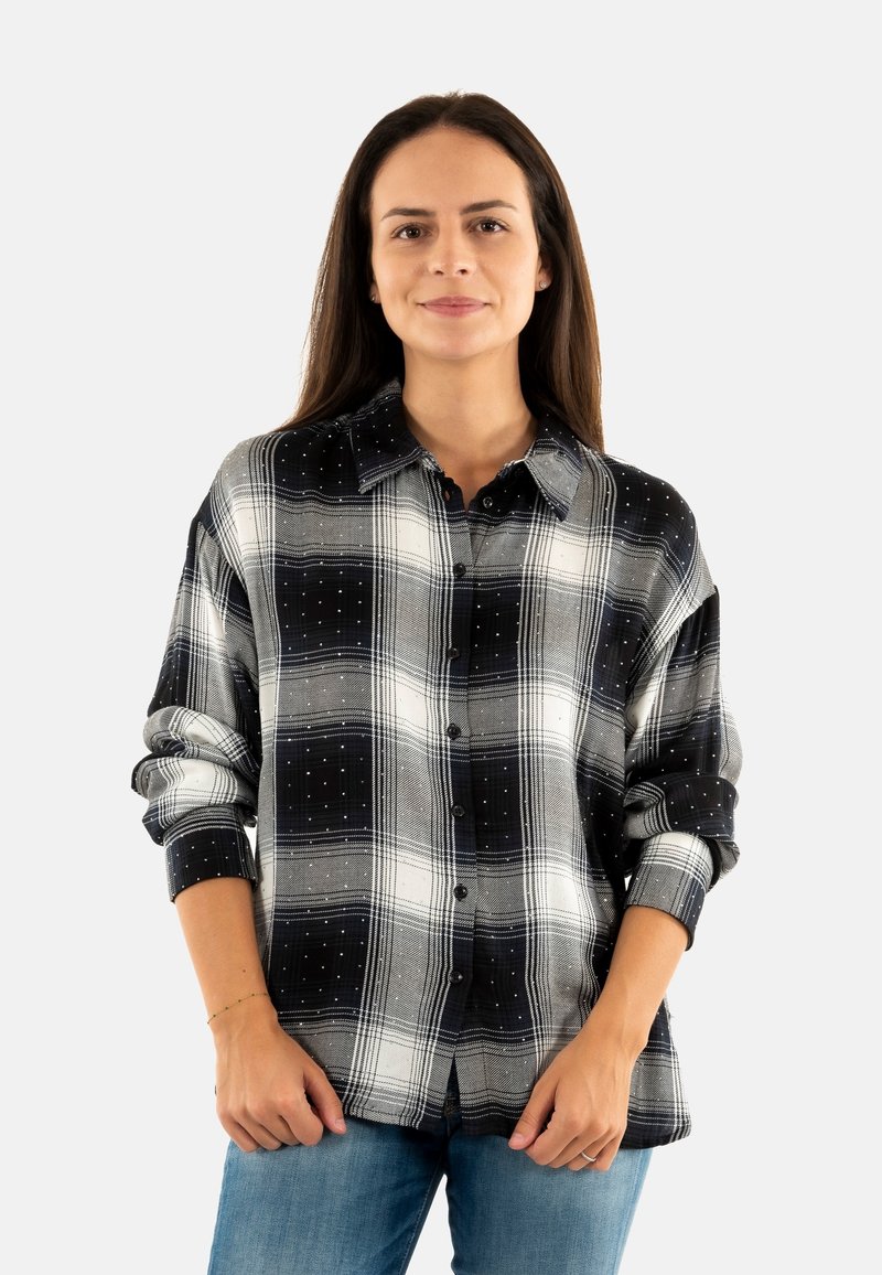 Camisa de franela a cuadros en blanco y negro con cuello redondeado, cierre de botones y sutiles adornos. Corte holgado con mangas arremangadas.