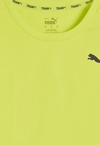 Erk kollaste Puma treeningpaita, mis on valmistatud tekstureeritud kangast. Omab ümarat kaelust ja musta Puma logo vasakul rinnakorvil.