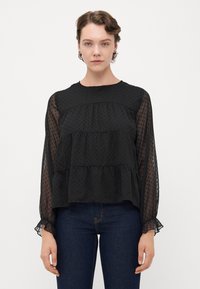 Schwarze, gestufte Bluse aus transparenter Stoff mit gepunkteter Textur. Verfügt über lange, leicht geraffte Ärmel und einen runden Ausschnitt.