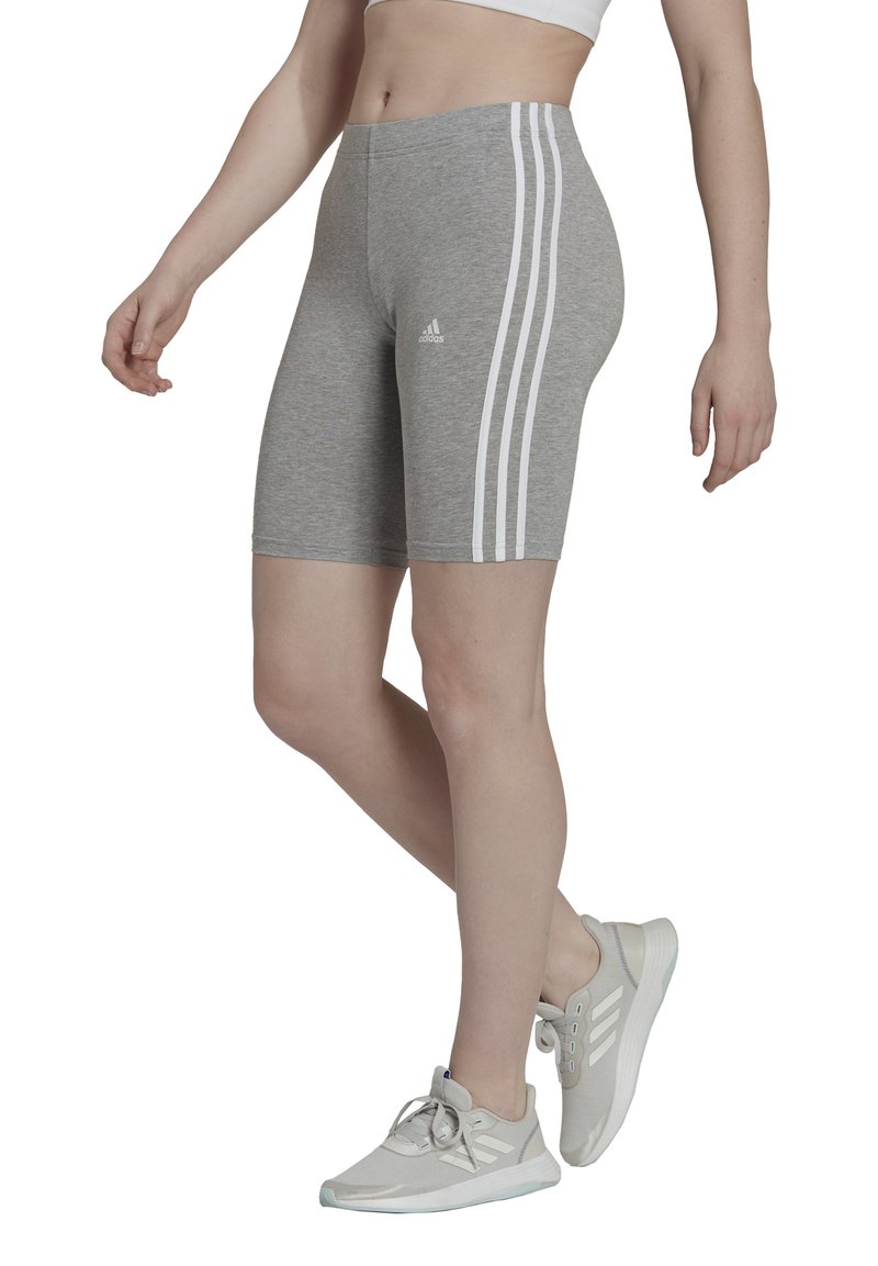 Grijze sportshorts met een witte drie-streepdesign aan de zijkanten, gemaakt van rekbaar materiaal. Gecombineerd met lichtgrijze sportschoenen.