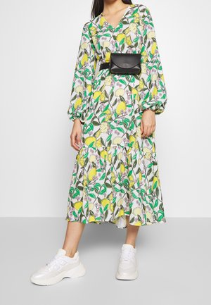 Vestido midi floral con un estampado de limones y bayas en amarillo, verde y blanco. Combinado con zapatillas blancas y un bolso de cintura negro.