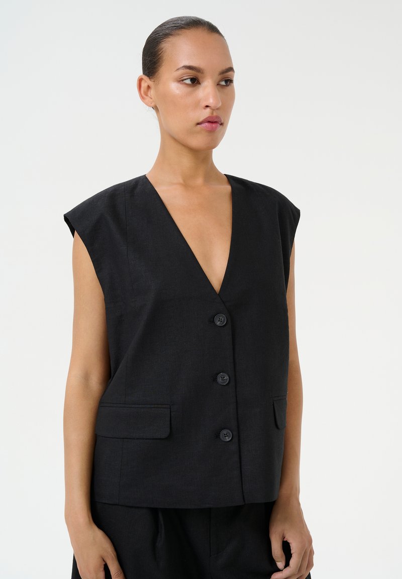 Črna brezrokavna jopica z globokim V-izrezom, petimi gumbi spredaj in dvema stranskima žepoma. Preprost, strukturiran dizajn in gladka tekstura.