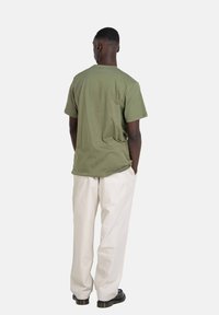 Olive green cotton t-shirt with short sleeves, relaxed fit, and round neckline, paired with cream-colored trousers and black shoes.