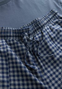 Blaues Baumwoll-T-Shirt kombiniert mit karierten Schlafanzughosen, die dunkelblauen und hellblauen Quadrate aufweisen, einen elastischen Bund sowie eine Kordel.