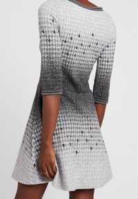 Robe à motif gris et noir, en tissu texturé, manches courtes, silhouette évasée avec encolure ronde et bordure décorative.