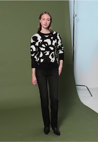 Pull à motifs noir et blanc avec une coupe ample, doté de manches longues et d'un col rond, associé à un jean slim noir et des bottines.