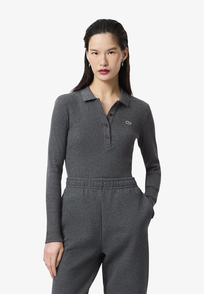 Polo gris à manches longues avec une texture côtelée, présentant une patte de boutonnage à trois boutons et un accent de logo vert sur la poitrine gauche.