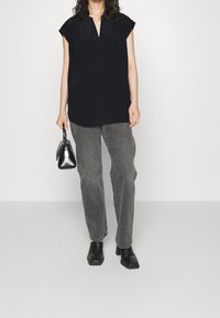 Top nero a maniche corte con scollo a V, abbinato a jeans grigi larghi e stivaletti neri con tacco quadrato. Borsa piccola in mano.