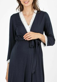 Robe avvolgente blu navy con maniche lunghe, caratterizzato da un bordo in pizzo bianco lungo il colletto e i polsini, legato in vita con una cintura abbinata.
