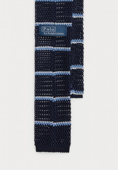 Tamsiai mėlyna megzta kaklaraištis su šviesiai mėlynomis ir baltomis juostelėmis, ant kaklaraiščio viršaus yra siuvinėtas "Polo by Ralph Lauren" etiketas.