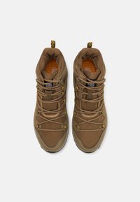 Ruskohitton kolmonen ruskeat vaelluskengät, joissa on tekstuurilla varustettu verkkopäällinen, pehmustettu kaulus, koristeelliset keltaiset yksityiskohdat ja kumipohja, jossa on pito-ominaisuuksia.