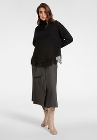 Czarny sweter polo z frędzlami, zestawiony z szarą asymetryczną spódnicą i beżowymi kozakami do kolan. Gładkie faktury, nowoczesny design.