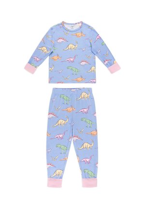 Junges Mädchen steht barfuß neben weißen Treppen, trägt blaue Pyjamas mit bunten Dinosauriermotiven und pinkfarbenen Bündchen.