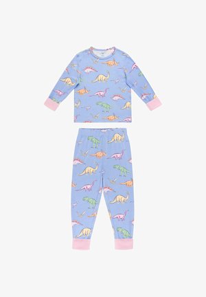 Ragazza giovane in piedi scalza accanto a scale bianche, che indossa un pigiama blu con stampe colorate di dinosauri e polsini rosa.