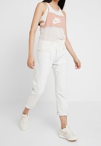 Lätt rosa och vit mesh-topp med Nike-logga, kombinerad med ljusa denimjeans med uppvikta ärmar och krämfärgade sneakers. Enkel, sportig stil.