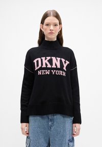 Czarny sweter z dzianiny z wysokim kołnierzem, z różowym napisem "DKNY NEW YORK". Żebrowane mankiety i dół dodają tekstury, a fason jest luźny.