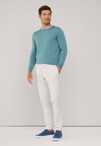 Lichtblauwe gebreide trui met witte kraag, witte broek en blauwe suède sneakers. Het ensemble is casual en getailleerd, met een gladde textuur.