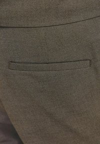 Smeđa teksturirana tkanina krojenih hlača s jednim horizontalnim džepom na stražnjoj strani, koji ima kontrastni obrub.
