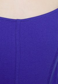 Fioletowa tkanina z prążkami z pionowym szwem biegnącym wzdłuż środka, o gładkiej strukturze i minimalistycznym designie.