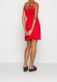 Robe rouge sans manches avec bretelles croisées dans le dos, taille élastique et jupe évasée ; associée à des sandales à plateforme noires.