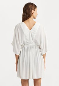 Vestido corto blanco con escote en V y mangas cortas y vaporosas. Presenta una cintura ajustada y una tela fluida con una sutil textura.