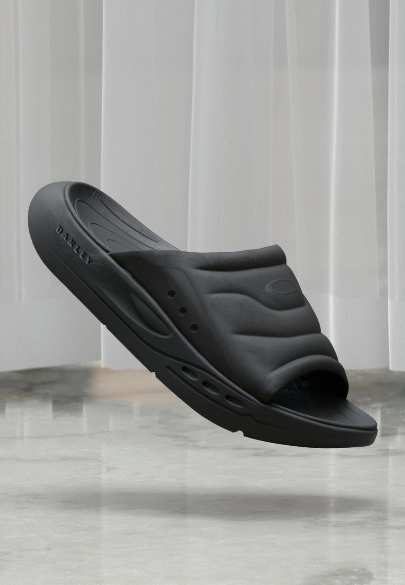 Czarne klapki z teksturowaną cholewką o falistym wzorze, w kształcie wsuwanek, z otworami wentylacyjnymi po bokach. Wykonane z elastycznego materiału.