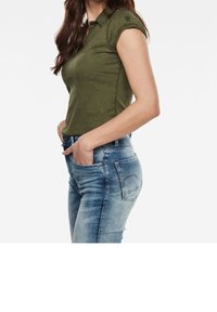 Olivgrön, figurnära polo med krage och korta ärmar, matchad med ljusblå denimjeans med klassisk femfickdesign.