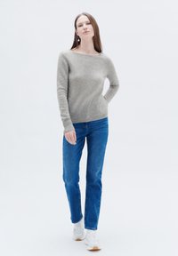 Maglione grigio chiaro a maglia con scollatura a barca, indossato con jeans blu a gamba dritta e sneakers bianche, che mettono in risalto una semplice e morbida texture.