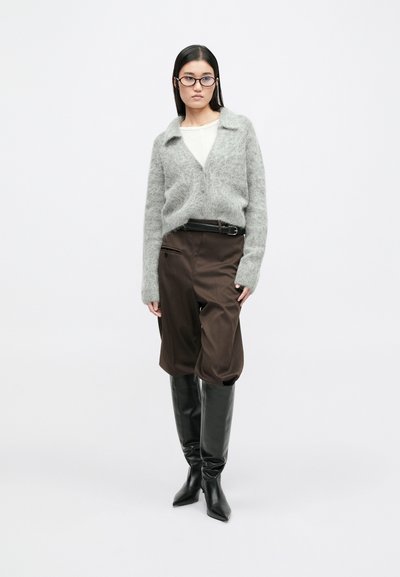 Szary puszysty kardigan, biały top, brązowe szerokie spodnie i czarne kozaki do kolan. Posiada kołnierzyk i detal w postaci paska.