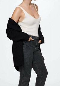 Černý oversized blejzr přes krémový ribbed top, doplněný o tmavě šedé džíny s vysokým pasem. Tkanina vypadá měkce s minimální texturou.