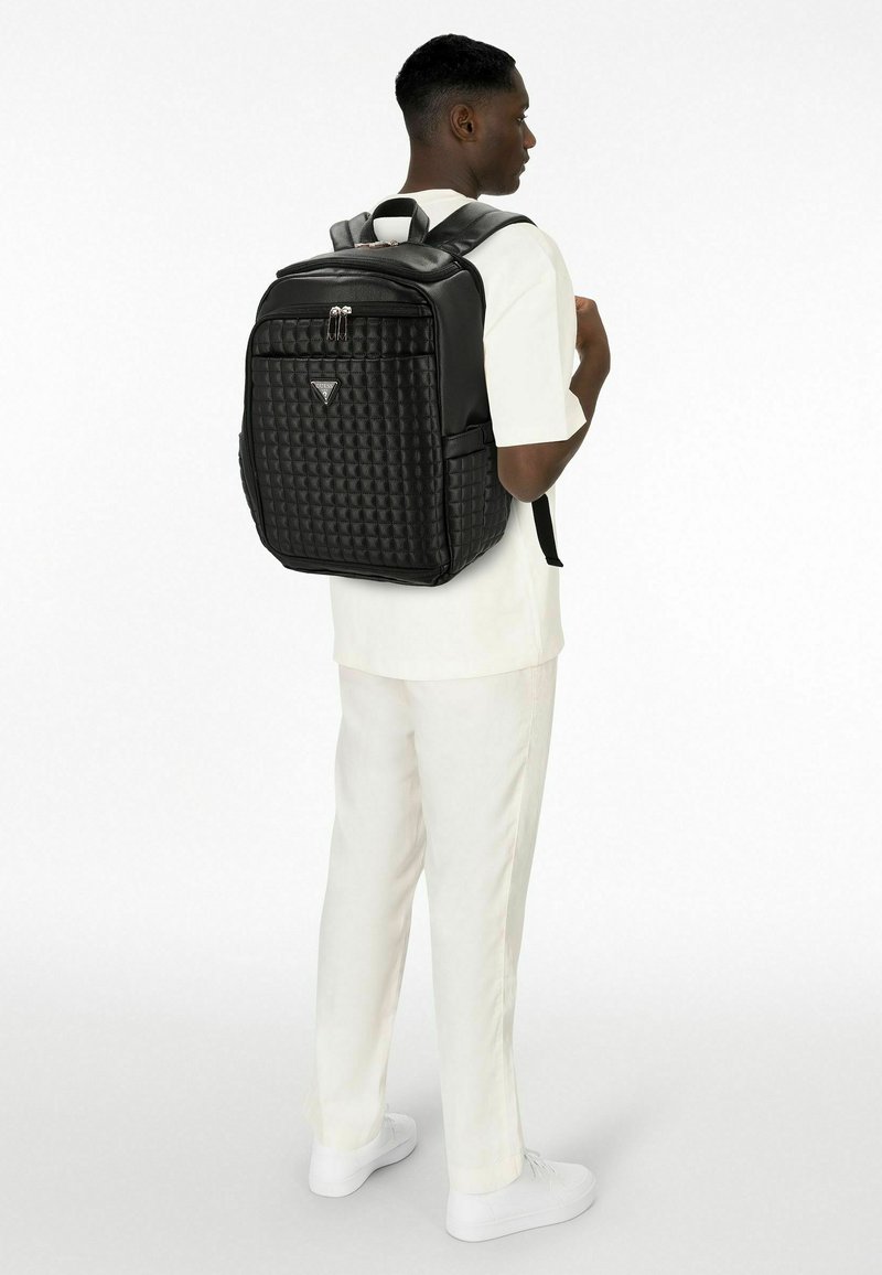 Zwarte gewatteerde rugzak van gestructureerd materiaal, voorzien van een zilveren logo, dubbele rits en verstelbare, gevoerde riemen.