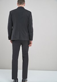 Schwarze Anzugjacke und passende Hose, Slim-Fit-Design, glattes Gewebe mit subtiler Textur, Rückansicht zeigt maßgeschneiderte Silhouette und klare Linien.